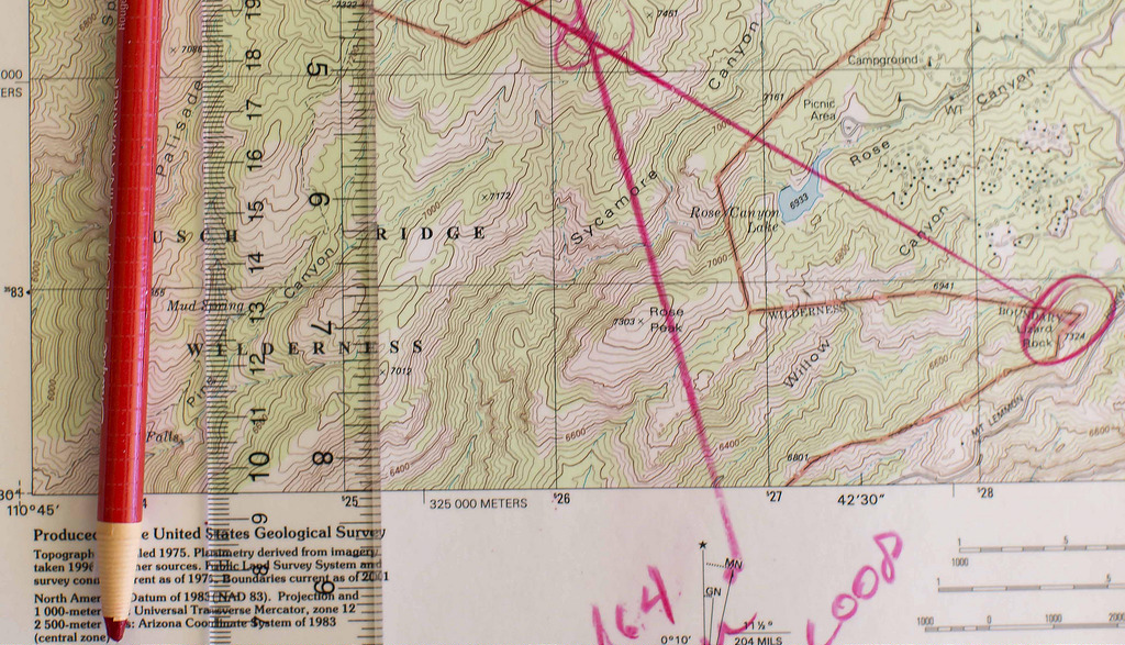 Topographical map marked up with red pencil, laying on the map with a ruler